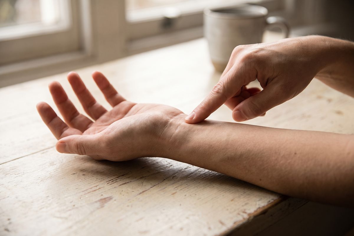 A hand resting palm up on a table while a finger points to a spot on the wrist.