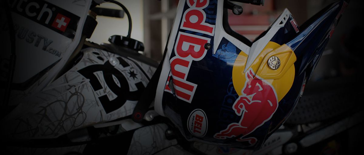 Robbie Maddison’s Bell helmet in Red Bull colours resting against the front number plate of his motocross bike, the DC and Rusty decals on the white plastics beside it.