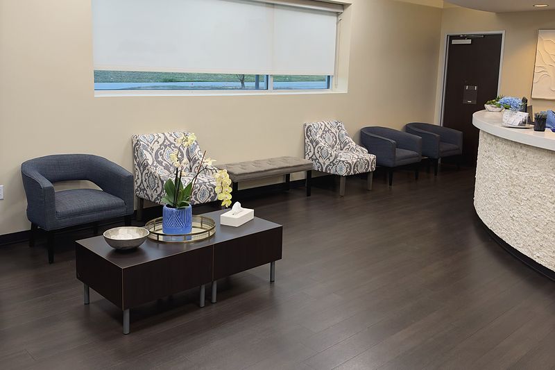 The waiting room at our Plano office, with blue armchairs, a low table and the curved reception counter on the right.