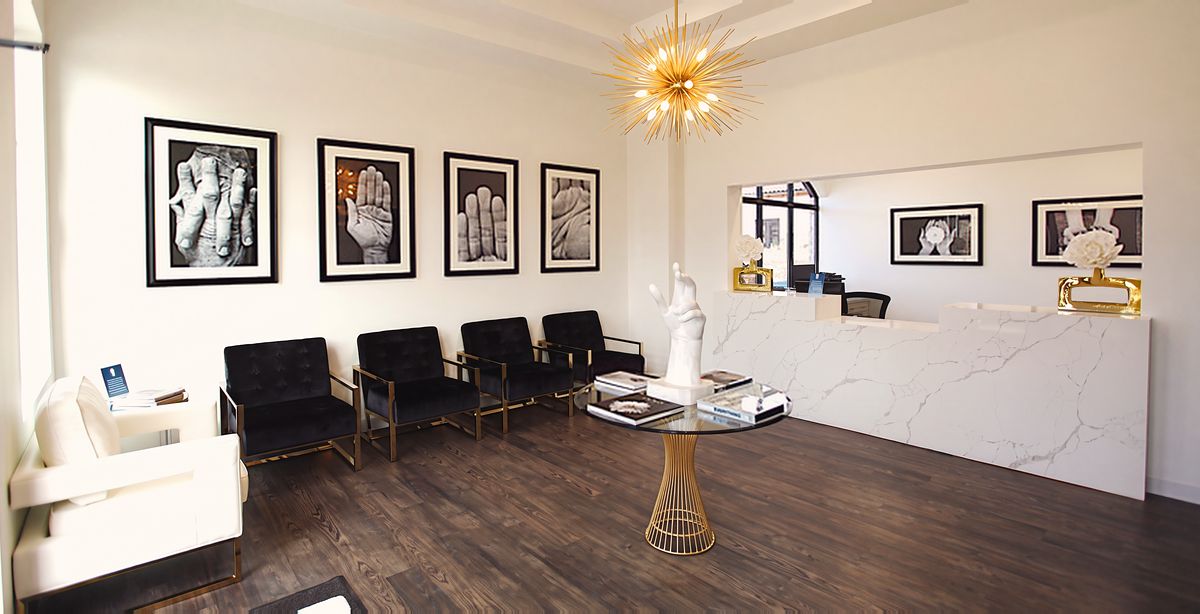 The waiting room at our Southlake office: four framed photographs of hands above the seating, the marble reception counter beyond and the hand sculpture on the table.