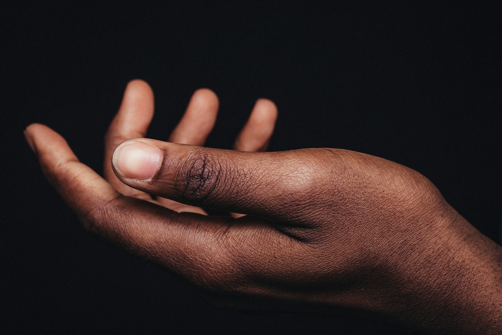 A hand held palm up with the fingers curled, lit against a black background.