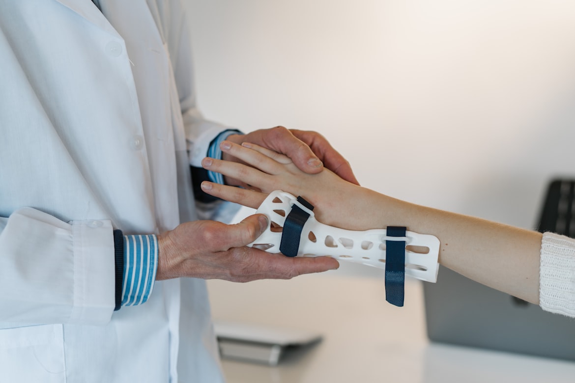 A clinician in a white coat fitting a white wrist splint to a patient's forearm.