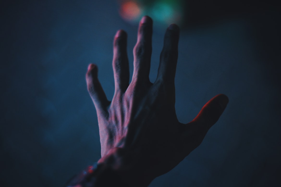 A hand held up with the fingers spread, lit in blue and red against a dark background.