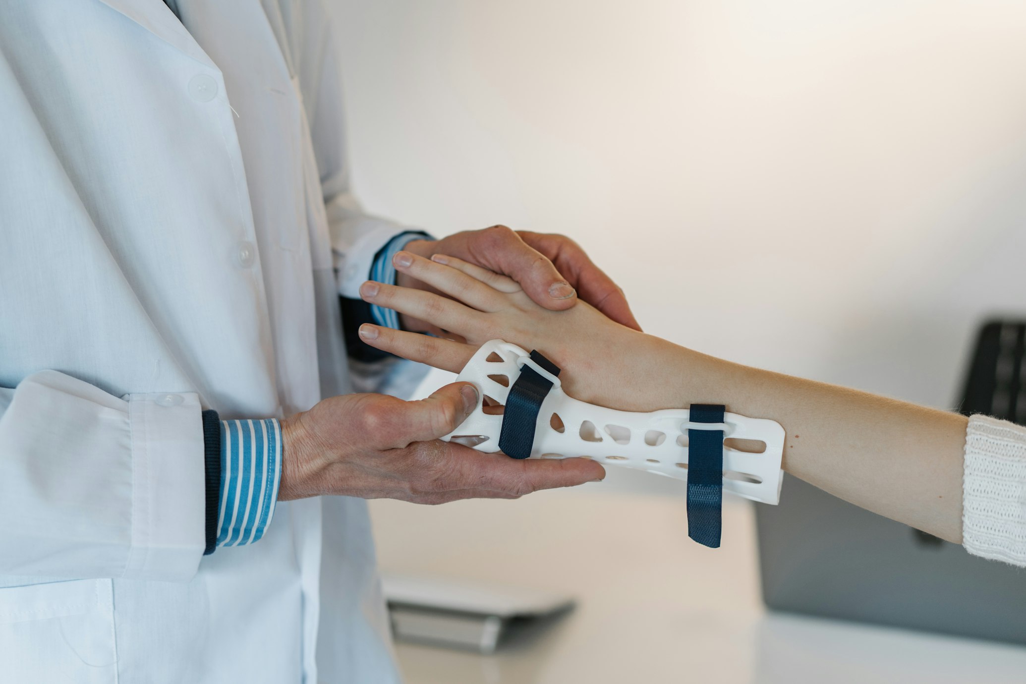 A clinician in a white coat fitting a white wrist splint to a patient's forearm.