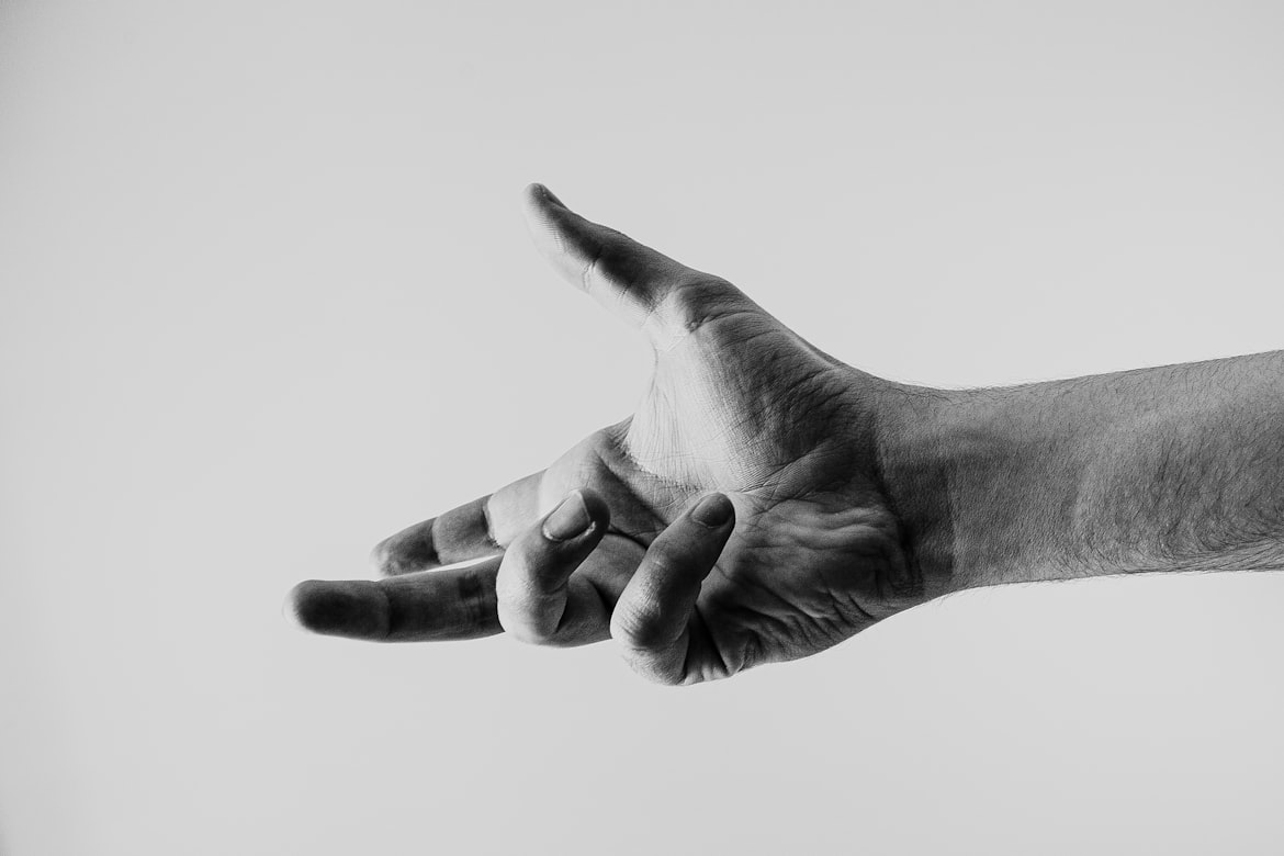 A black and white photograph of a hand reaching forward with the fingers spread.