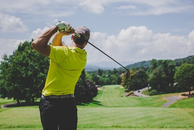 A golfer at the top of the follow-through on a fairway, hills in the distance.